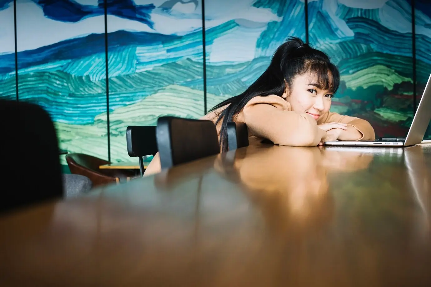 Ein Mädchen liegt mit einem Laptop auf einem Tisch.